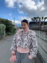 Person wearing a leopard print sweater with a pink shirt underneath, standing outdoors on a street.